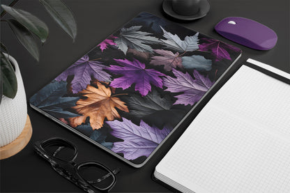 Leaf-patterned laptop skin on a desk with a notebook, glasses, and mouse.
